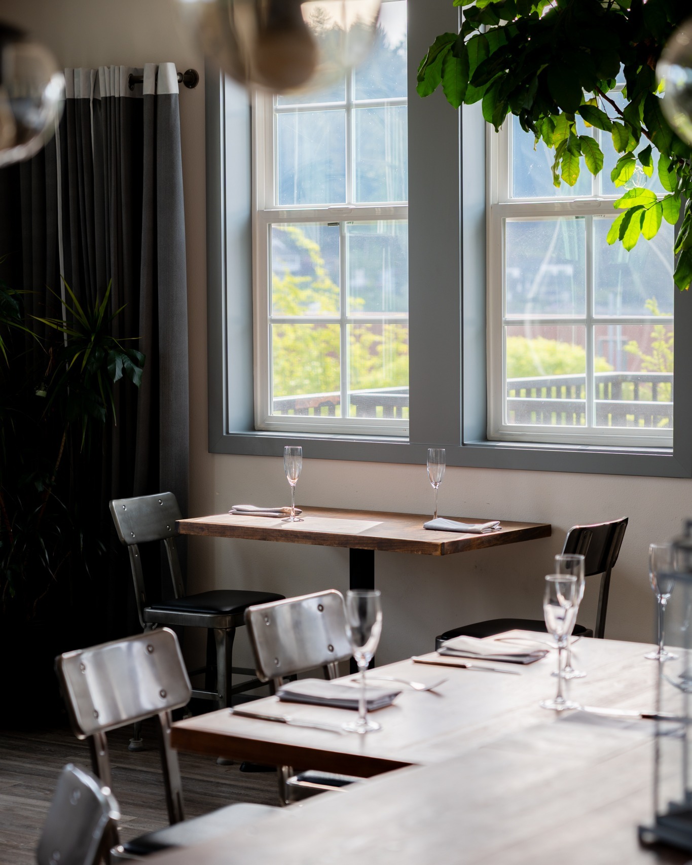 A window table set for two in the Brix 25° dining room, sunlight and greenery beyond the paned windows