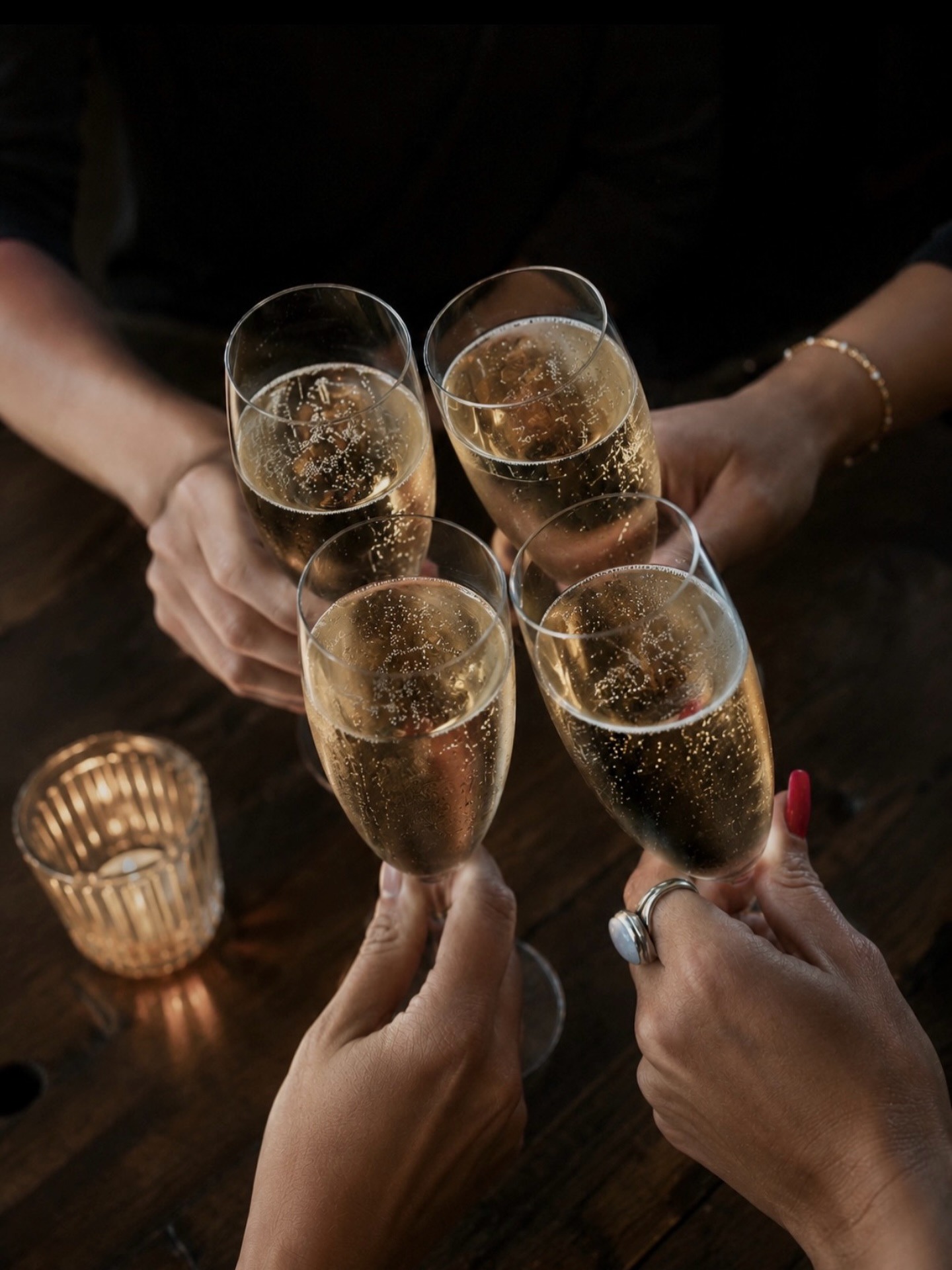 Four hands raising glasses of sparkling wine in a toast over a candlelit table at Brix 25°