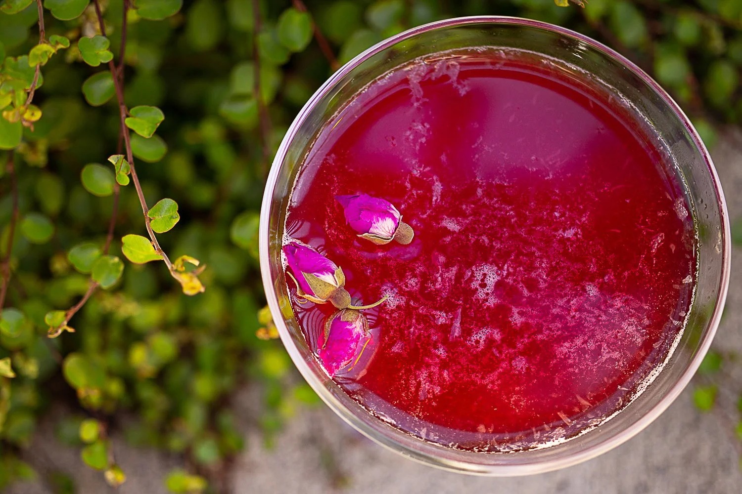 A jewel-toned handcrafted cocktail garnished with rose buds