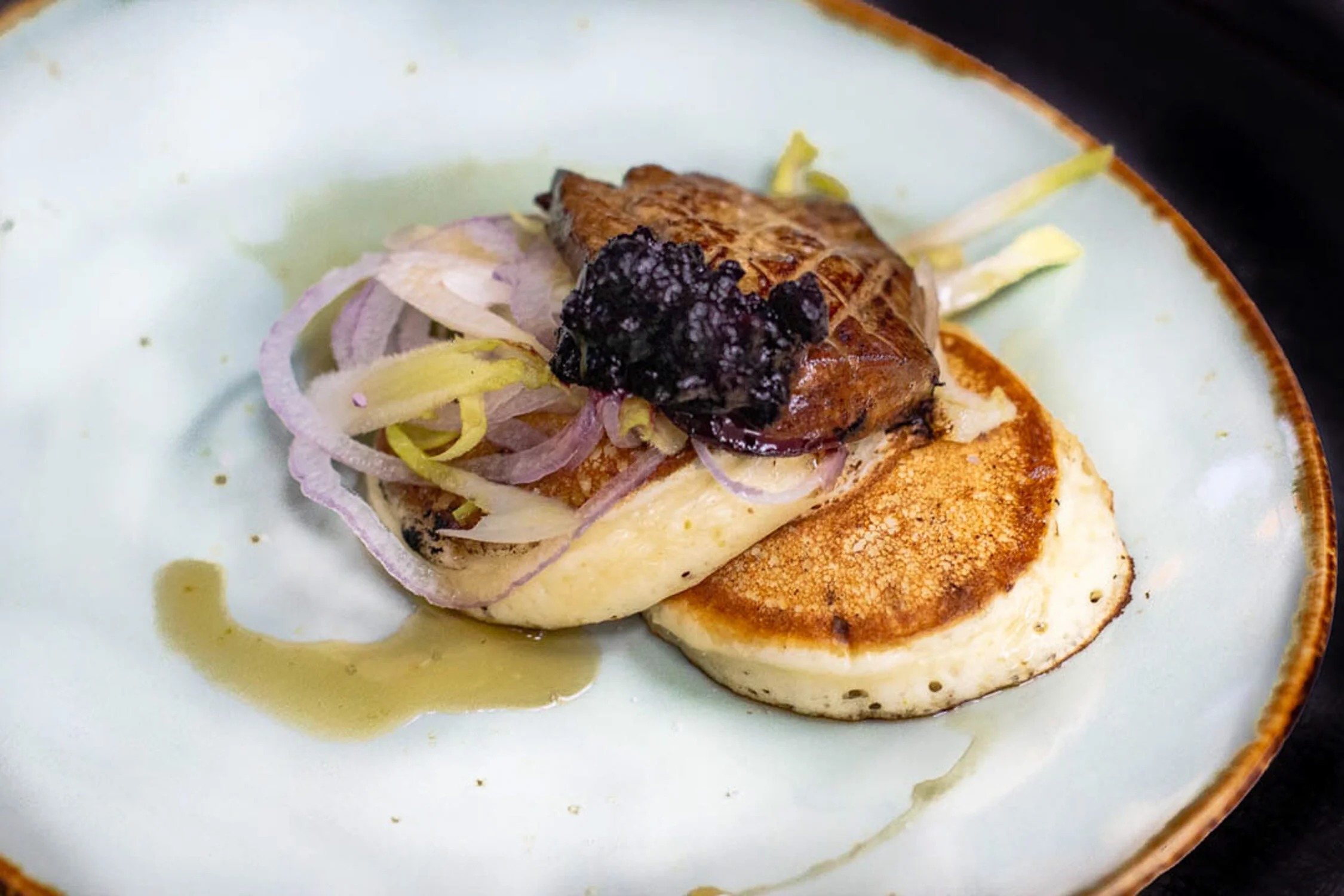 A seared course over house blini with pickled shallot and blackberry