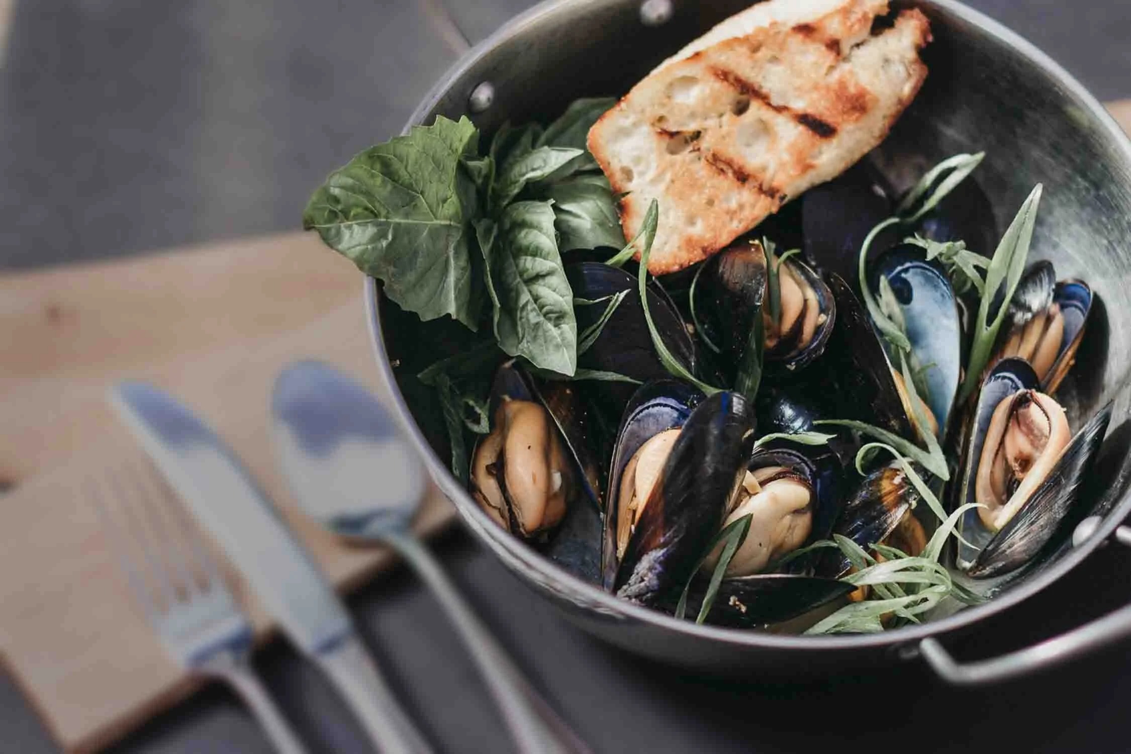 Steamed mussels with fresh herbs and grilled bread in a copper pot
