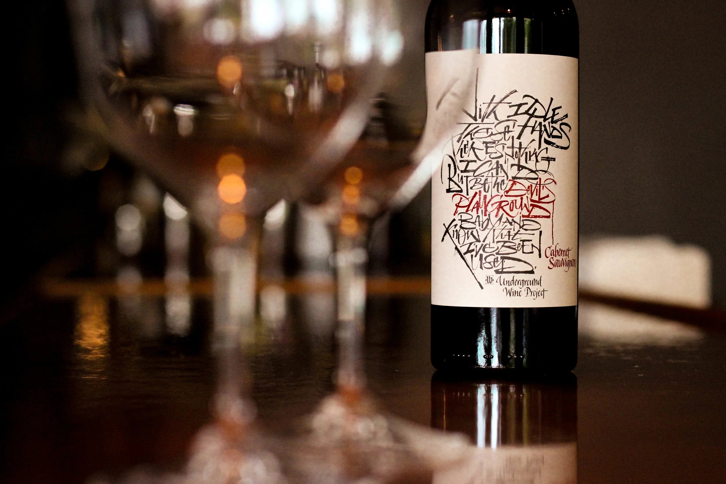 A bottle of Cabernet Sauvignon beside wine glasses in warm candlelight at the Brix 25° bar